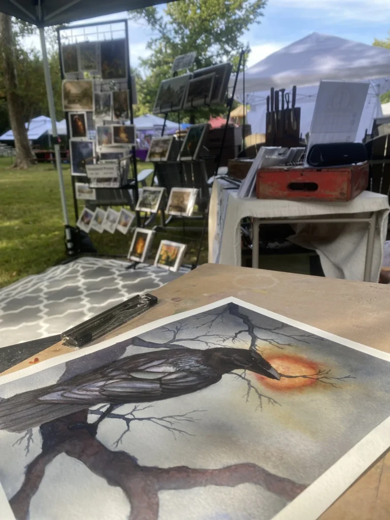 Black Sentinel watercolor on a worktable at the CRAW booth, with art displays and forged objects behind it.